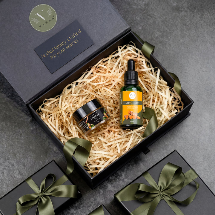 Gift set with a bottle and jar in a black box with straw filler on a gray surface.