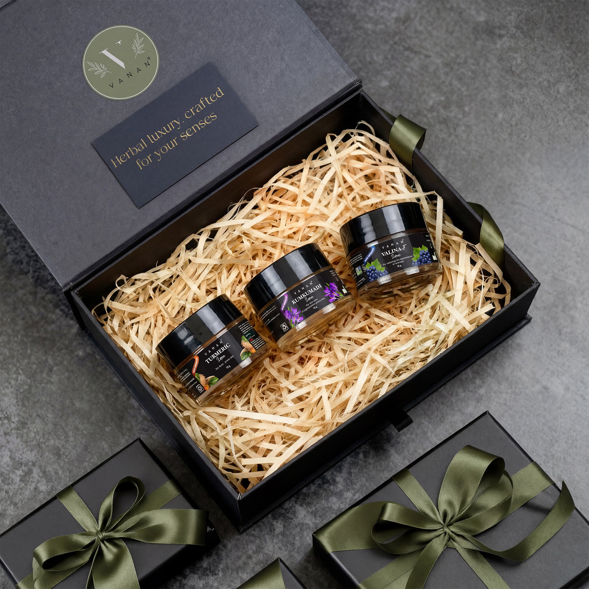 Three jars in a black gift box with decorative ribbons on a gray surface
