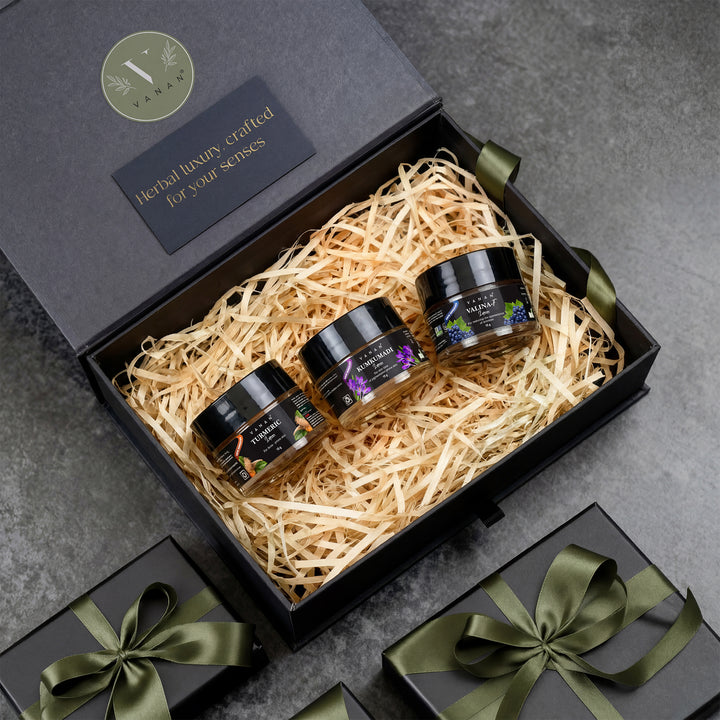 Three jars in a black gift box with decorative ribbons on a gray surface